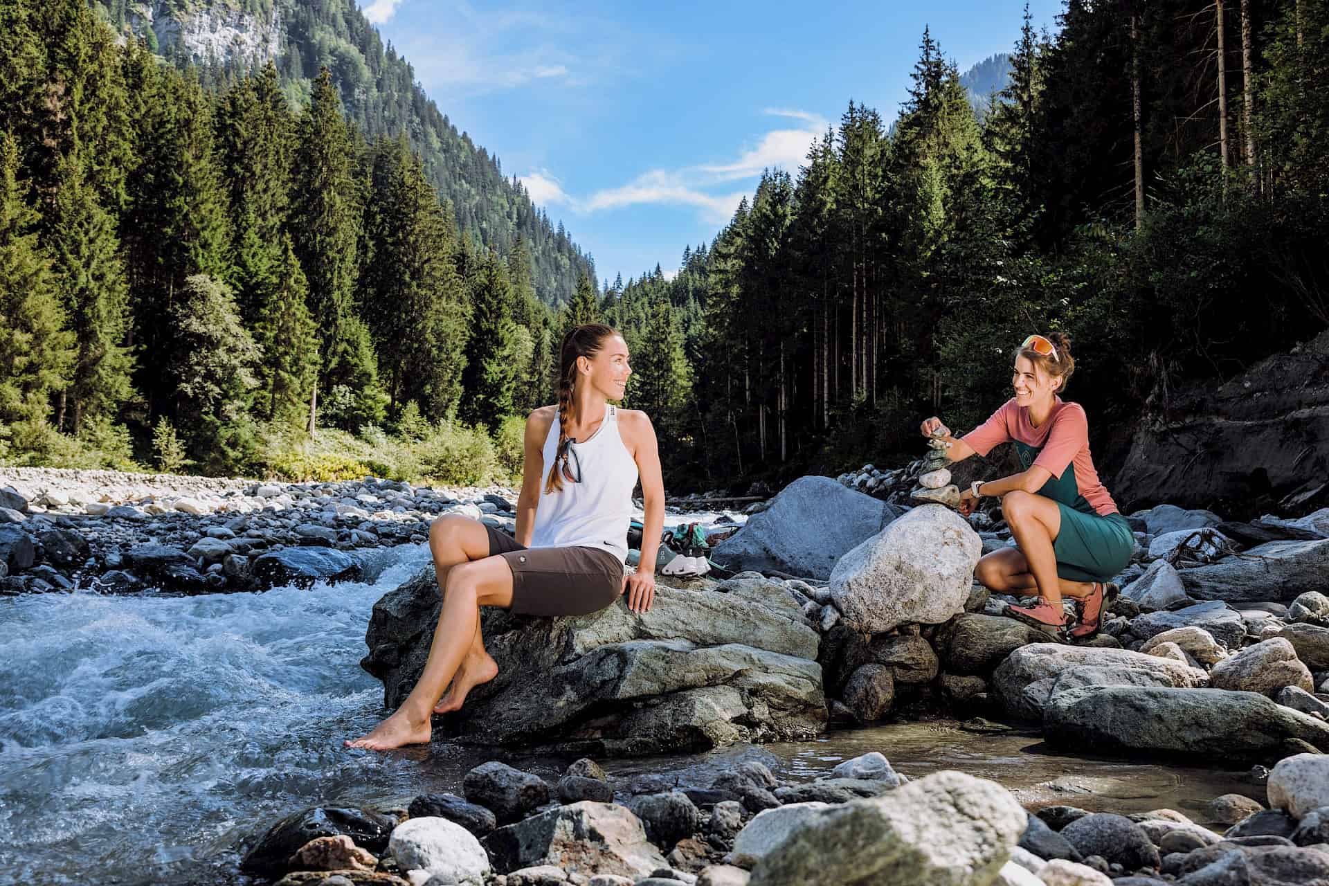 Dvě ženy si užívají pauzu u horského potoka v idylickém údolí Habachtal ve Wildkogel Areně, obklopeny lesy a horami.
