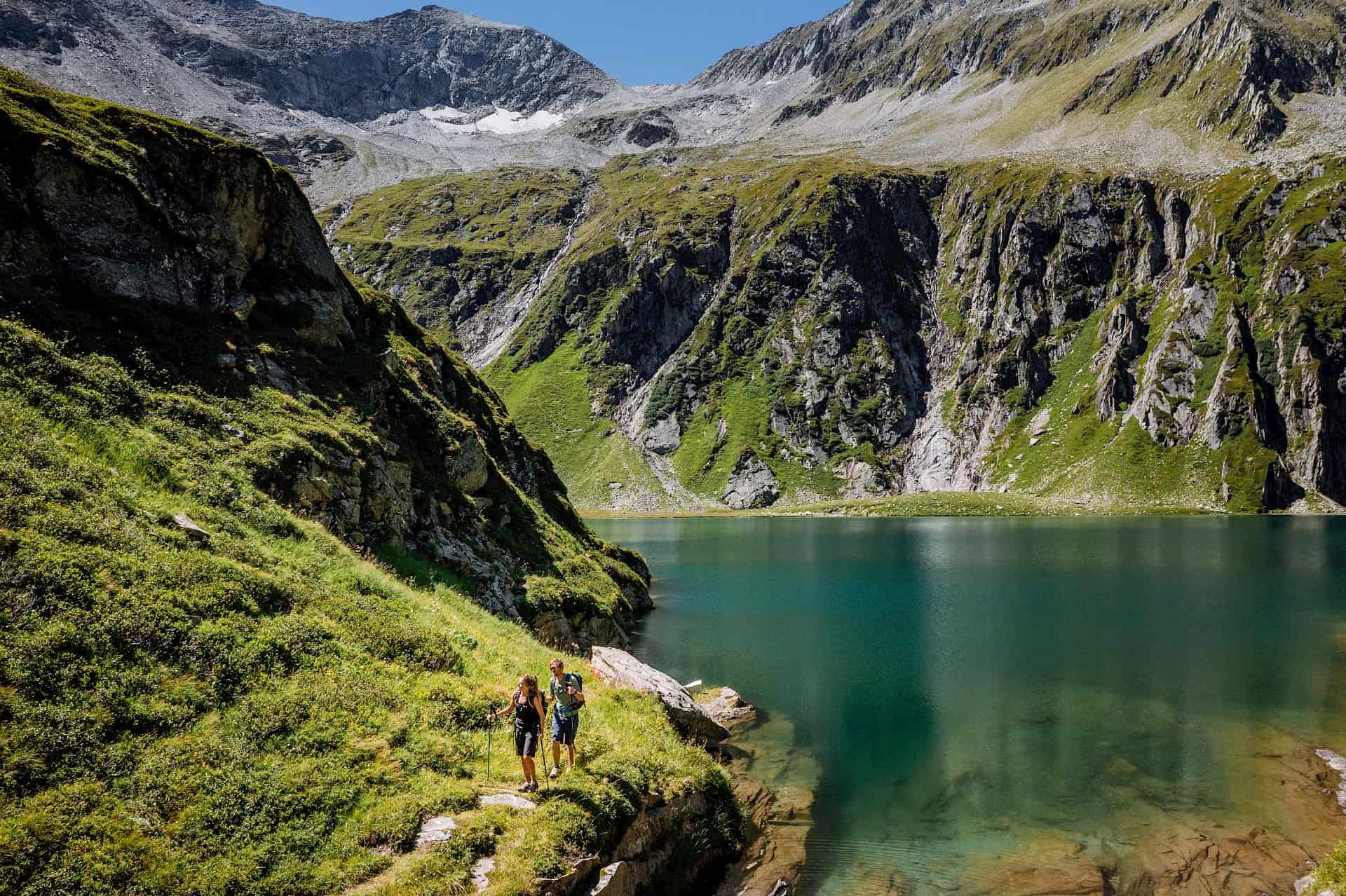 Wanderer am kristallklaren Seebachsee im Nationalpark Hohe Tauern, umgeben von beeindruckenden Bergen und alpiner Natur. Eine traumhafte Wanderung in der Wildkogel-Arena – ideal für Naturliebhaber und Bergbegeisterte im SalzburgerLand.